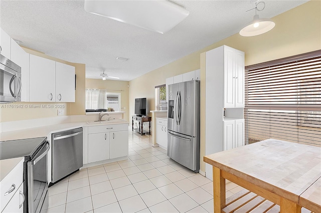 kitchen with light countertops, light tile patterned floors, white cabinets, stainless steel appliances, and a sink