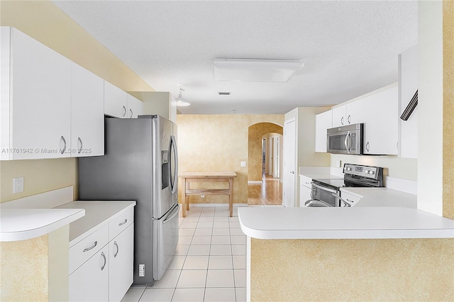 kitchen featuring a textured ceiling, arched walkways, appliances with stainless steel finishes, light tile patterned flooring, and light countertops