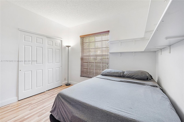 bedroom featuring a closet, baseboards, a textured ceiling, and light wood-style floors