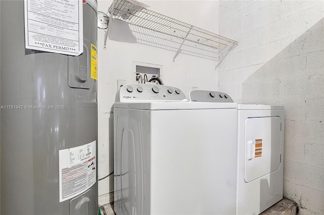 clothes washing area featuring concrete block wall, electric water heater, independent washer and dryer, and laundry area