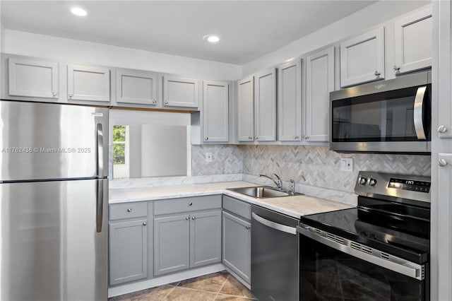 kitchen featuring decorative backsplash, recessed lighting, gray cabinets, stainless steel appliances, and a sink