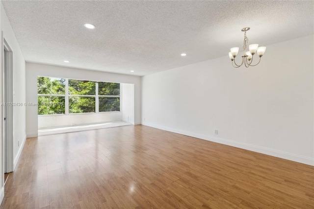 spare room featuring a notable chandelier, a textured ceiling, wood finished floors, recessed lighting, and baseboards