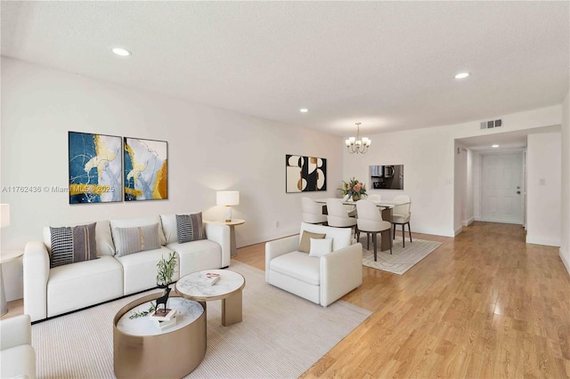 living area with visible vents, a textured ceiling, a chandelier, and light wood-style flooring