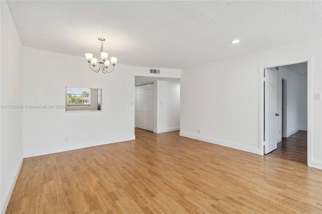 empty room featuring light wood-type flooring, visible vents, a textured ceiling, baseboards, and a chandelier