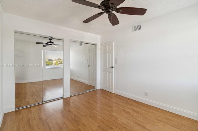 unfurnished bedroom featuring visible vents, multiple closets, a textured ceiling, wood finished floors, and baseboards