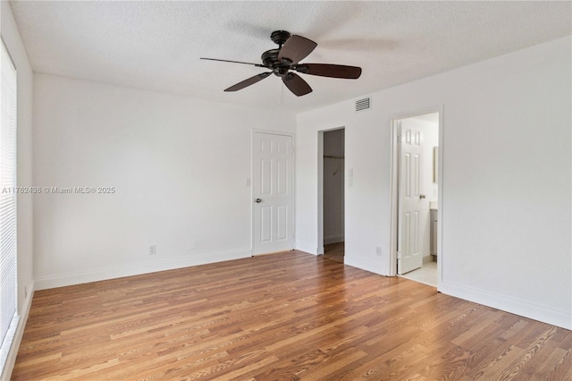 unfurnished bedroom featuring baseboards, visible vents, light wood finished floors, a spacious closet, and a textured ceiling