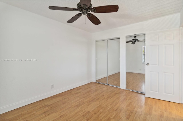 unfurnished bedroom with multiple closets, light wood-style flooring, a ceiling fan, a textured ceiling, and baseboards