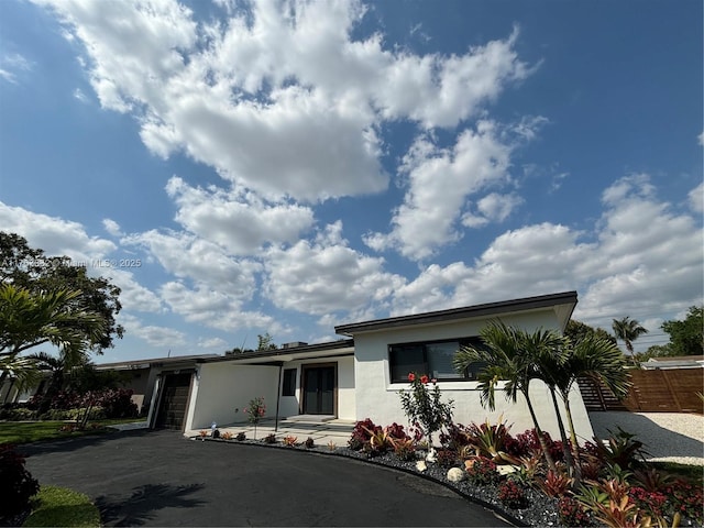 view of front of property featuring stucco siding, an attached garage, driveway, and fence