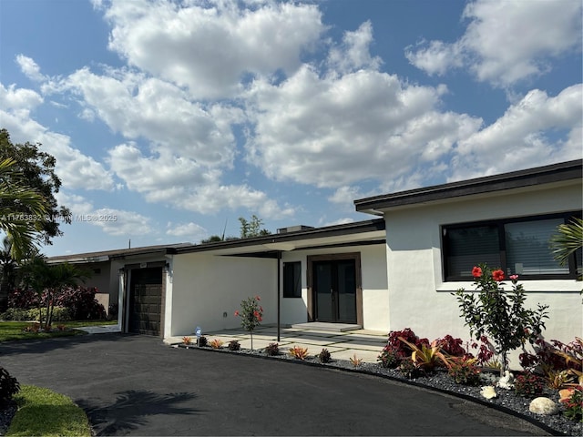 view of front of property with aphalt driveway, stucco siding, an attached garage, and french doors