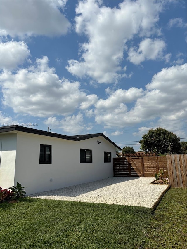 rear view of property featuring a yard, fence, and stucco siding