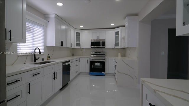 kitchen featuring a sink, appliances with stainless steel finishes, white cabinets, decorative backsplash, and light stone countertops