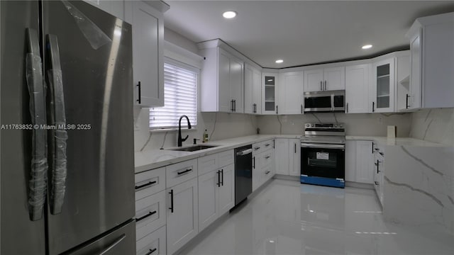 kitchen featuring light stone counters, white cabinetry, stainless steel appliances, and a sink