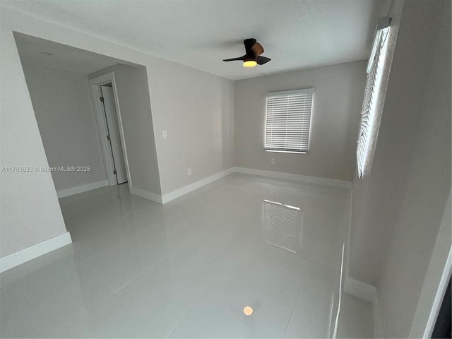 unfurnished room with light tile patterned floors, a ceiling fan, and baseboards