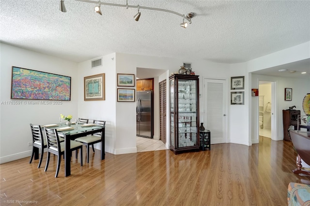 dining room featuring a textured ceiling, baseboards, visible vents, and light wood-type flooring