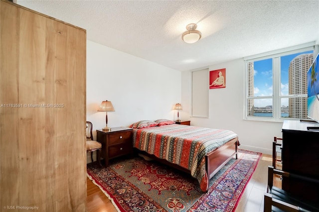 bedroom featuring baseboards, a textured ceiling, and wood finished floors