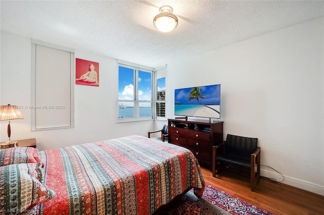 bedroom featuring baseboards, a textured ceiling, and wood finished floors