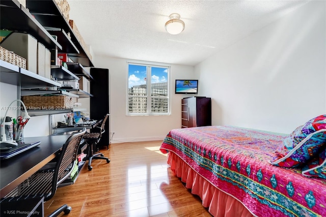 bedroom featuring baseboards, a textured ceiling, stainless steel refrigerator with ice dispenser, and light wood finished floors