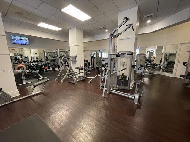 exercise room with visible vents, a paneled ceiling, a high ceiling, and wood finished floors