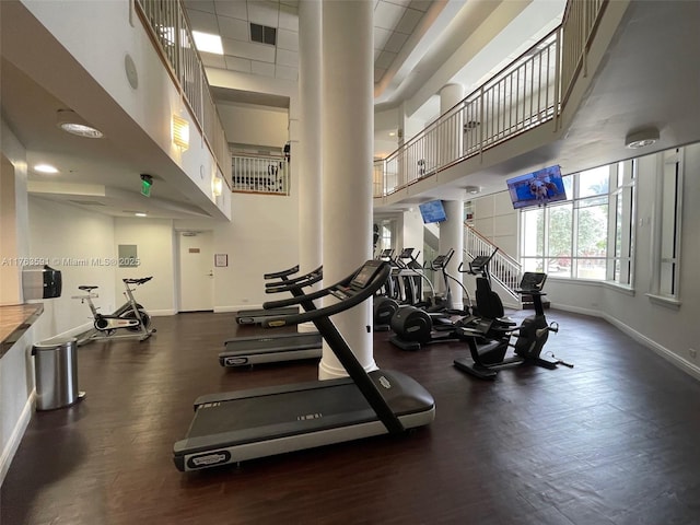 exercise room with wood finished floors, visible vents, baseboards, ornate columns, and a high ceiling