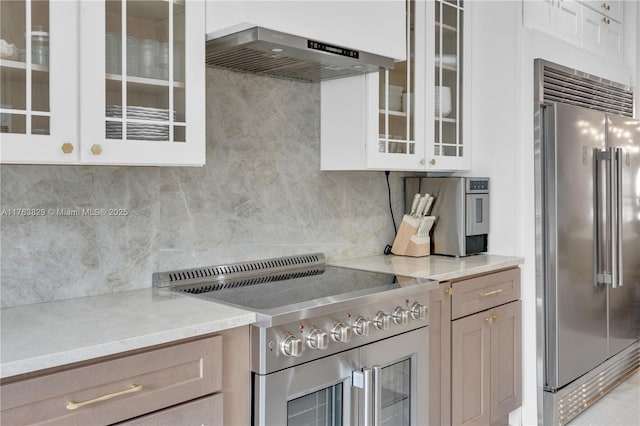 kitchen featuring glass insert cabinets, backsplash, high end appliances, and wall chimney range hood