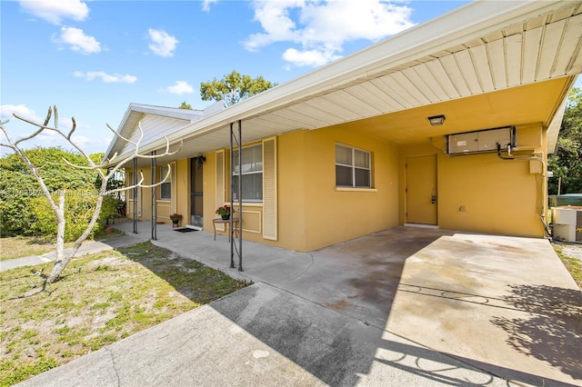 view of exterior entry with a carport, stucco siding, driveway, and central AC