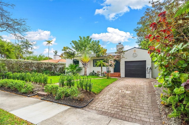 view of front of home featuring a front yard, stucco siding, a chimney, decorative driveway, and a garage