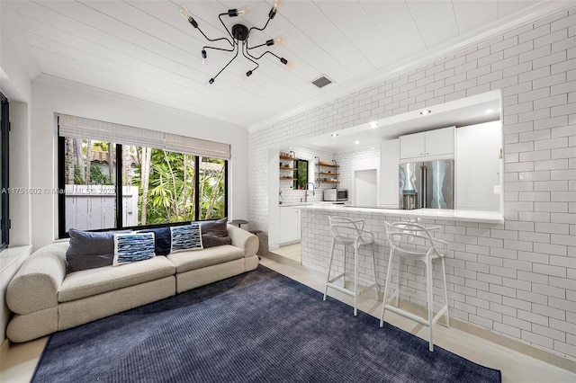 unfurnished living room featuring visible vents, brick wall, crown molding, and a sink