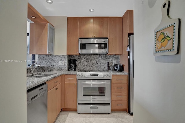 kitchen featuring a sink, stainless steel appliances, light stone counters, and decorative backsplash