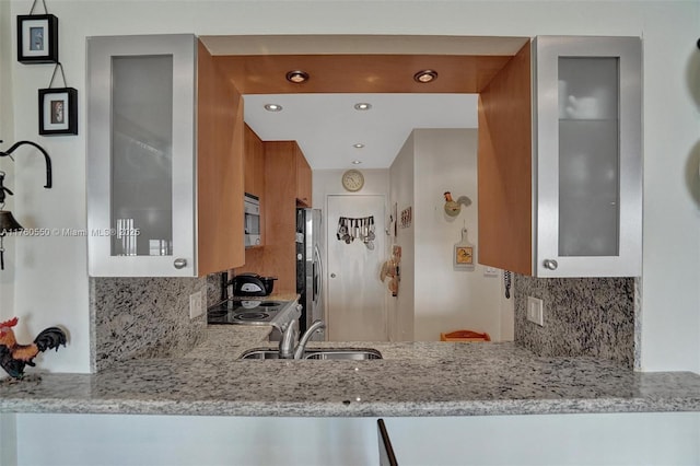 kitchen featuring light stone counters, glass insert cabinets, stainless steel appliances, and a sink