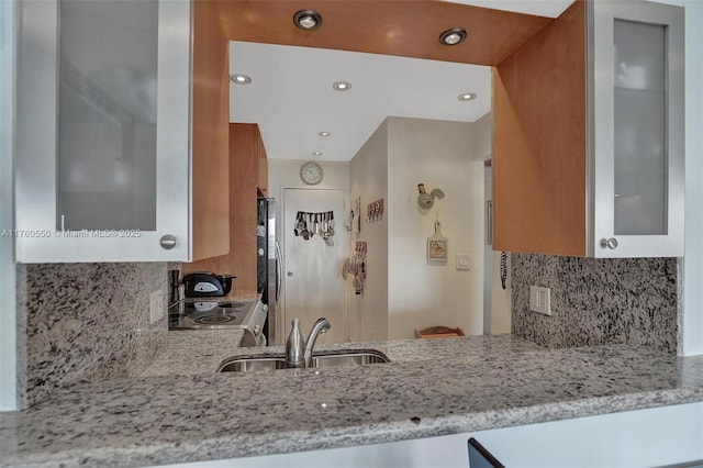 kitchen featuring glass insert cabinets, light stone countertops, brown cabinetry, electric range, and a sink