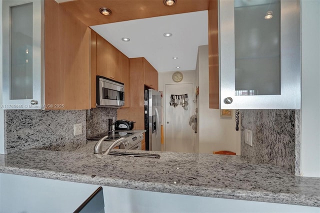 kitchen with a sink, light stone counters, brown cabinets, and stainless steel appliances