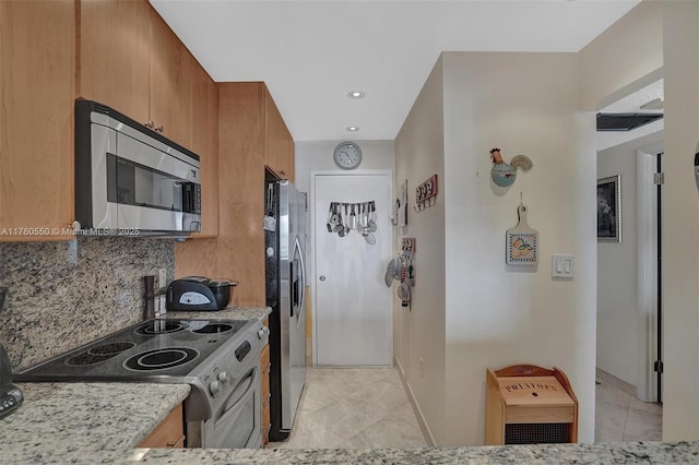 kitchen with light tile patterned floors, light stone countertops, brown cabinetry, stainless steel appliances, and backsplash