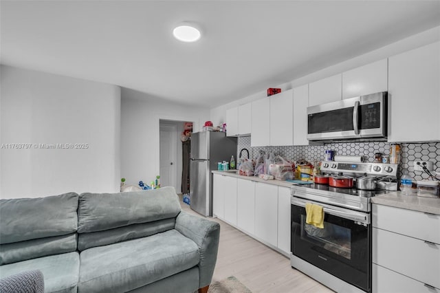 kitchen with light wood-type flooring, backsplash, white cabinetry, stainless steel appliances, and light countertops