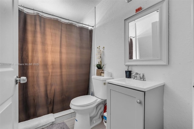 full bathroom with toilet, vanity, and a textured wall