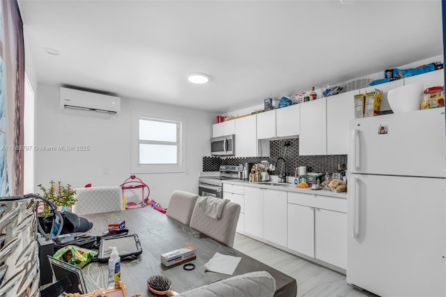 kitchen with a sink, backsplash, a wall unit AC, appliances with stainless steel finishes, and light countertops