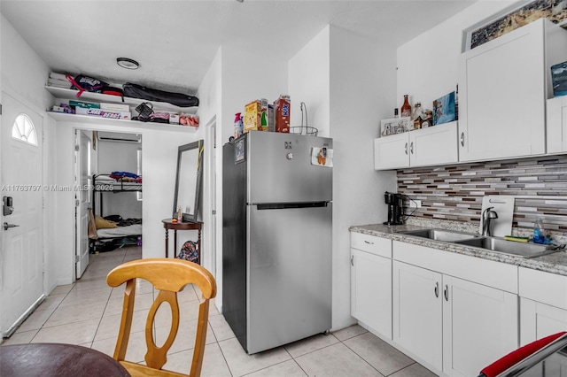 kitchen featuring light tile patterned flooring, freestanding refrigerator, a sink, white cabinets, and tasteful backsplash