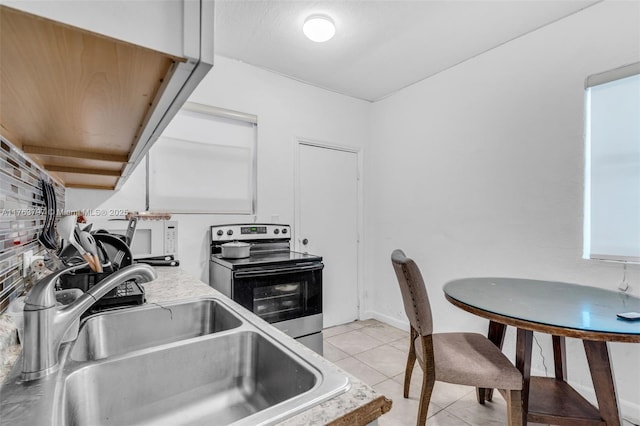 kitchen with white microwave, light countertops, light tile patterned floors, stainless steel range with electric cooktop, and a sink