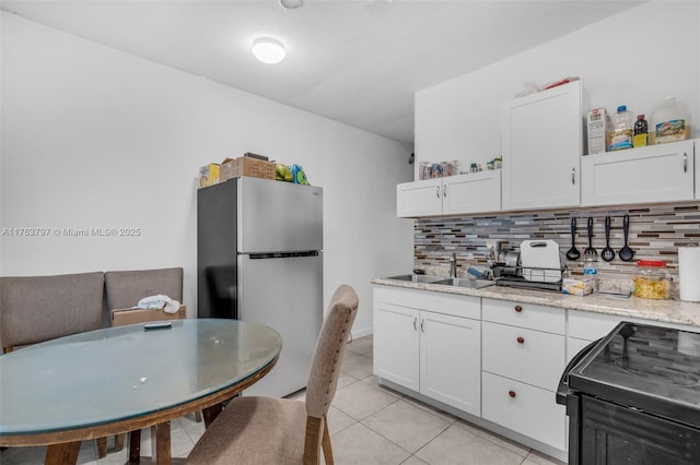 kitchen with backsplash, black range with electric cooktop, white cabinets, and freestanding refrigerator