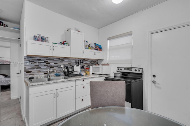 kitchen with white microwave, tasteful backsplash, electric stove, white cabinetry, and a sink