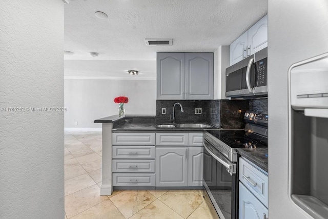 kitchen with visible vents, a sink, backsplash, appliances with stainless steel finishes, and a peninsula