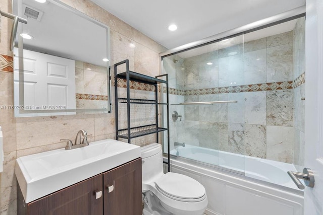 bathroom featuring visible vents, toilet, vanity, shower / bath combination with glass door, and tile walls