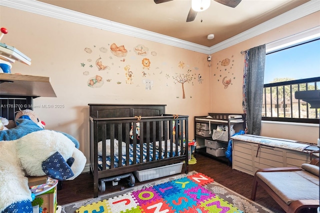 bedroom with crown molding, a nursery area, wood finished floors, and ceiling fan