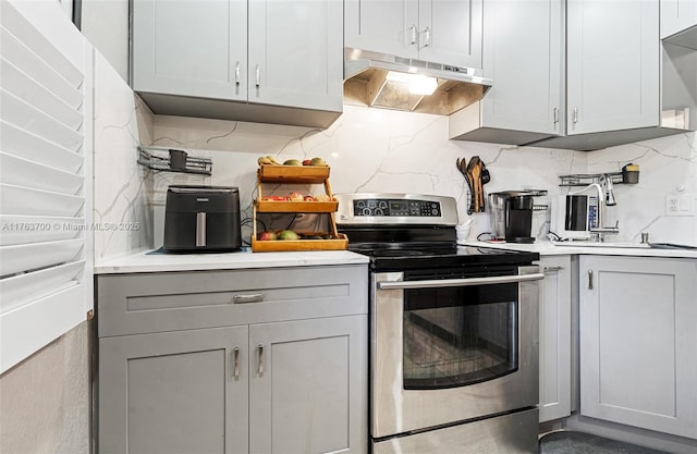 kitchen with gray cabinetry, light countertops, electric stove, under cabinet range hood, and backsplash