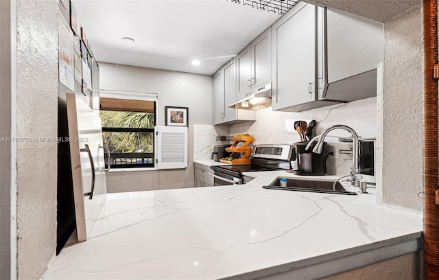 kitchen with light stone counters, electric stove, under cabinet range hood, and a sink