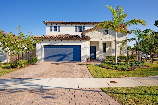 mediterranean / spanish-style home with stucco siding, decorative driveway, stone siding, fence, and a tiled roof