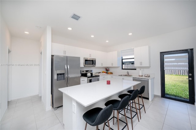 kitchen with a kitchen island, a sink, stainless steel appliances, light countertops, and a kitchen bar