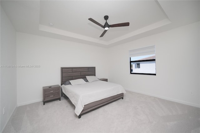 carpeted bedroom with baseboards, a raised ceiling, and a ceiling fan