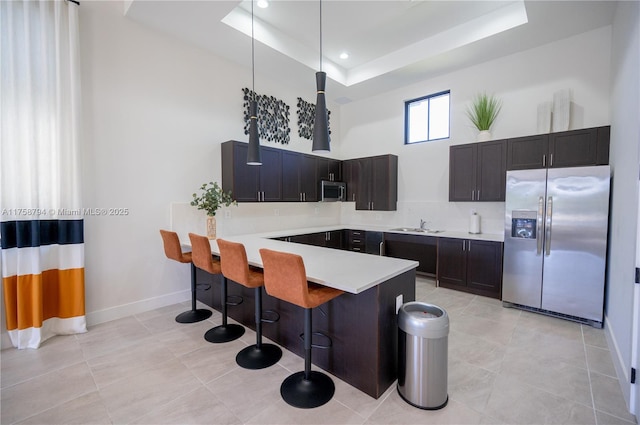 kitchen featuring a breakfast bar, a peninsula, a tray ceiling, light countertops, and appliances with stainless steel finishes