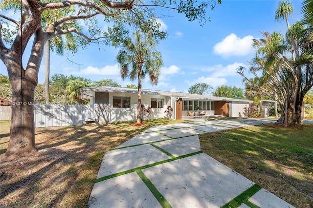 ranch-style home featuring concrete driveway, fence, a front lawn, and stucco siding