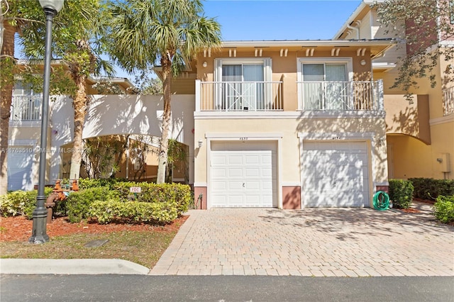 view of front of home featuring a balcony, decorative driveway, a garage, and stucco siding